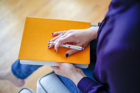 Close-up of woman holding bright orange notebook and pen