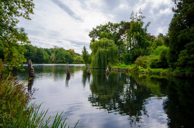 Peaceful lakeside park with lush greenery and artistic sculptures in the water. Ideal for nature enthusiasts, landscape design presentations, peacefulness, and relaxation themes.