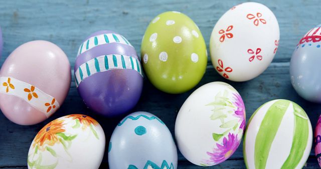 Brightly colored Easter eggs with various artistic patterns and designs spread out on a blue wooden table. This image is perfect for Easter-themed promotions, holiday decorations, social media posts, festive greeting cards, and spring crafts ideas.
