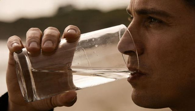 Man drinking water from glass at seaside closeup with droplets, reflections, calm contemplative gaze