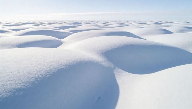 Undulating snow mounds casting blue shadows across minimalist arctic winter plain