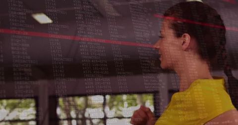 Woman in yellow top studying redacted data on glass lobby display and futuristic interface