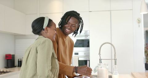 African American couple cooking together at bright modern kitchen island smiling warmly