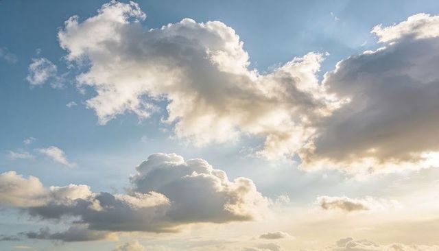 Golden Sunlight Drifting through Towering Cumulus Clouds over Expansive Blue Sky