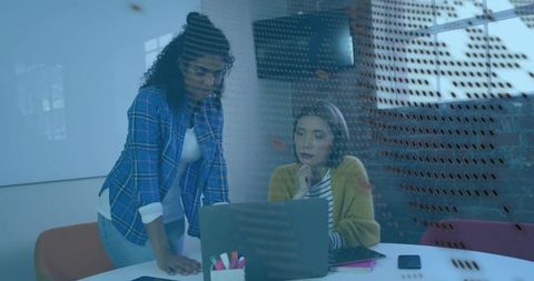 Collaborating Women Leaning Over Laptop in Modern Office Through Glass Partition