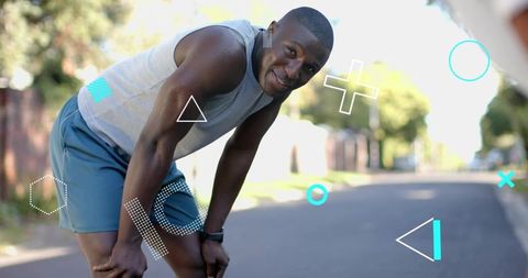 Smiling runner bending hands-on-knees pausing during neighborhood run wearing fitness watch
