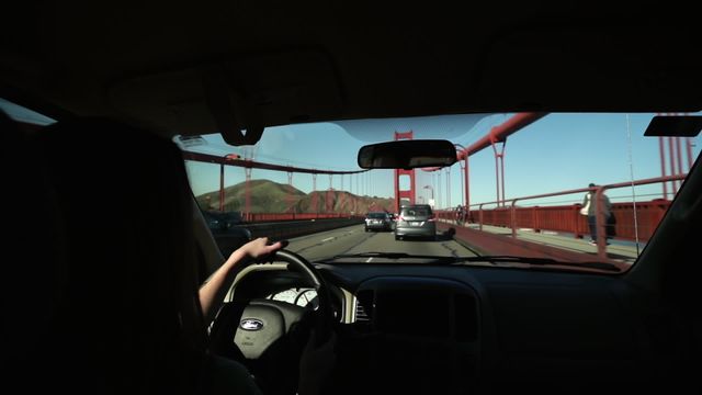 Over the shoulder view of a young Caucasian woman driving a car on the Golden Gate Bridge, San Francisco