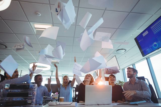 Business team celebrating success by tossing papers in the air. Ideal for depicting corporate achievements, teamwork, and a positive work environment. Suitable for use in business presentations, corporate websites, and promotional materials highlighting team spirit and workplace happiness.