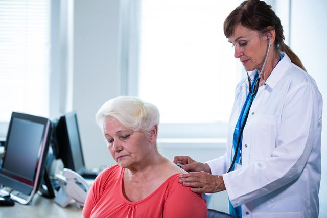 Female doctor using stethoscope to examine senior patient in hospital. Ideal for healthcare, medical services, elderly care, doctor-patient relationships, and health checkup related content.
