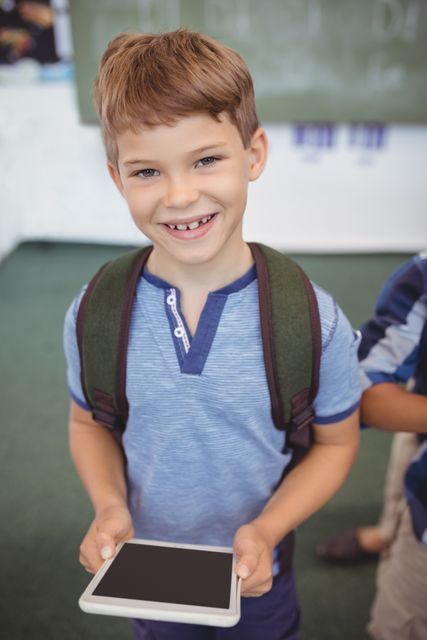 Portrait of cute schoolboy standing with digital tablet I school