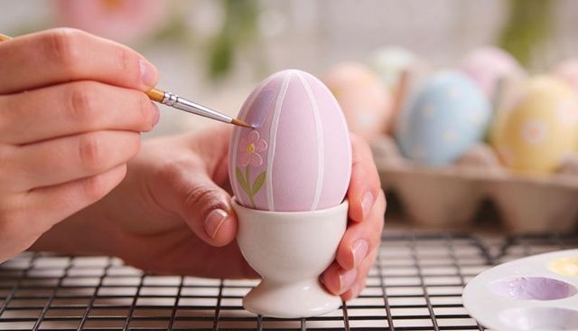 Hand painting pastel easter egg with floral motif using fine brush and ceramic egg cup