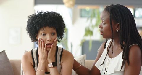 African american women sharing emotional support on sofa, comforting friend at home