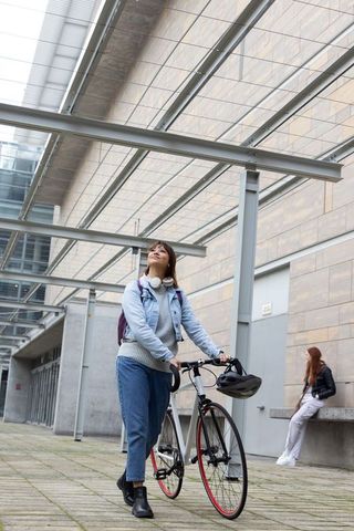 Young woman walking and holding road bicycle under modern canopy wearing denim jacket