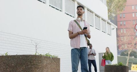 African American commuter checking phone with headphones on urban sidewalk near brick wall