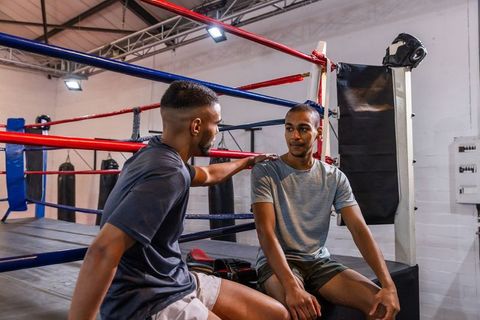 Two african american men sitting in boxing ring corner, one placing hand on shoulder