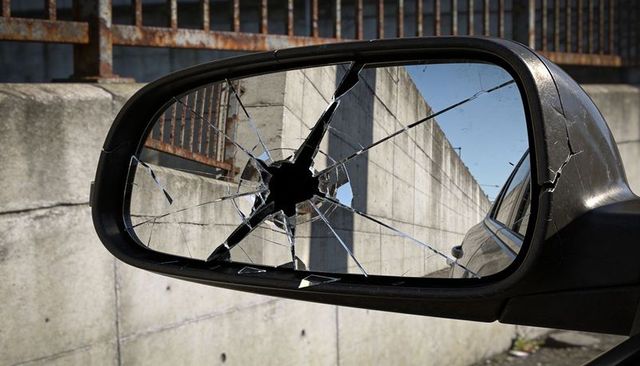 Shattered car side mirror with star-shaped hole and cracked glass against concrete wall