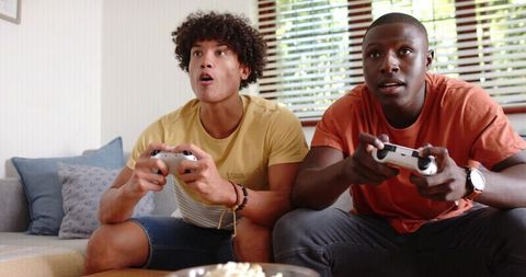 Friends competing in video game session on couch with white controllers in cozy living room
