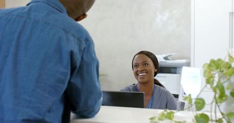 Smiling african female receptionist welcoming visitor at modern clinic front desk