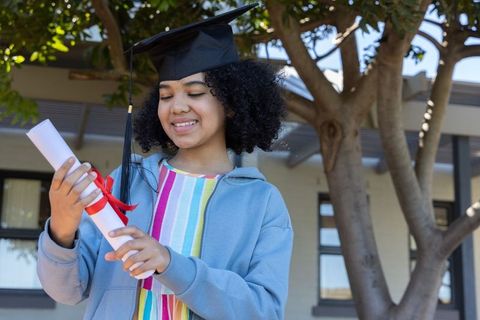 African american teen graduate holding diploma with mortarboard celebrating achievement