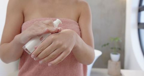 Woman Applying Lotion in Bright, Minimalist Bathroom