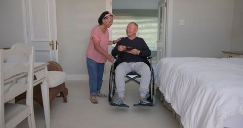Asian woman assisting elderly man in wheelchair in home environment