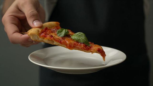 Hand holding margherita pizza slice over white plate with fresh basil
