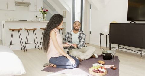 Happy Couple Celebrating with Gift Exchange on Picnic Blanket in Modern Home