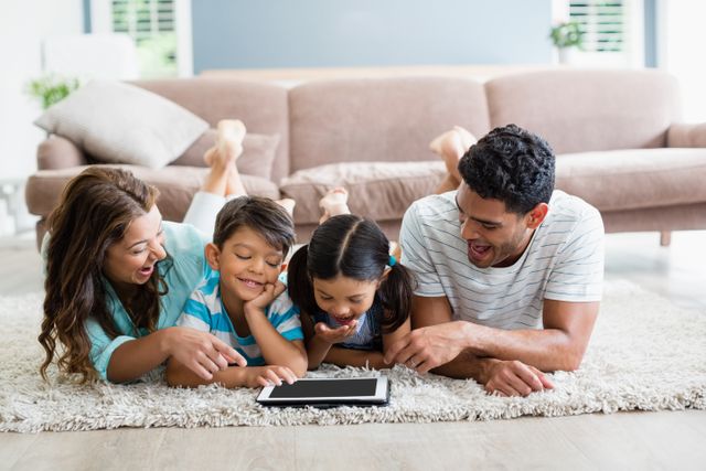 Parents and children lying on rug and using digital tablet in living room at home