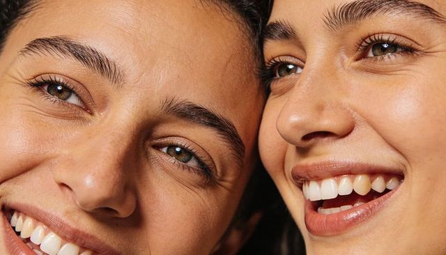 Smiling women pressing cheeks together closeup showing eyes, teeth, brows, natural skin texture