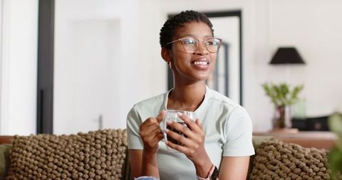 Smiling woman sipping coffee on sofa in modern cozy living room interior