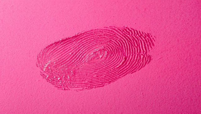 Closeup fingerprint leaving glossy residue on magenta textured paper, macro detail