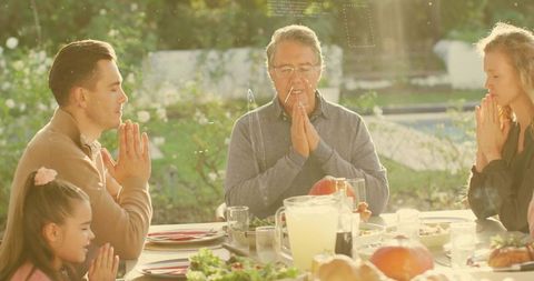 Multigenerational Family Praying at Outdoor Dinner Table During Golden Hour