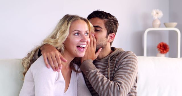 Young Man Whispering in Girlfriend's Ear on Sofa - Download Free Stock Images Pikwizard.com