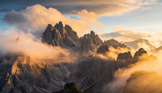 Golden dawn lighting jagged alpine spires piercing low clouds over remote peaks