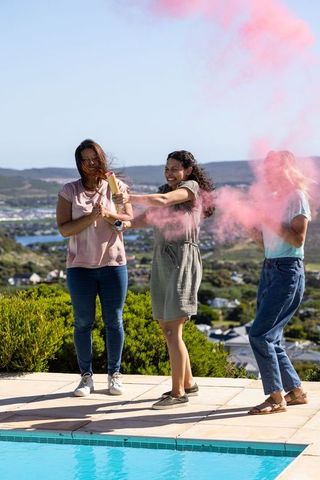 Diverse Female Friends Playing with Pink Smoke Near Cozy Pool
