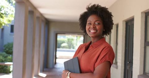Confident african woman standing on campus walkway holding tablet smiling, professional
