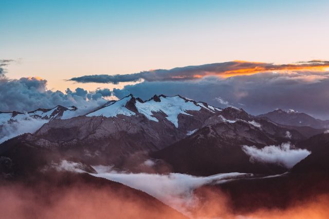 Ideal for travel and nature-related content, this image features snow-covered mountains during sunrise with clouds creating a dramatic effect. It can be used for promoting travel destinations, adventure activities, mountain hiking tours, and nature conservation campaigns.