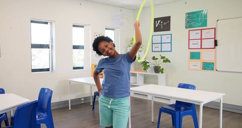African girl holding neon hula hoop in bright classroom smiling and playing