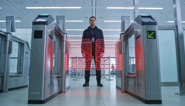Man standing at airport security turnstiles with red laser grid scanning and access control tech