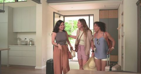 Diverse women arriving at modern vacation rental carrying luggage and summer accessories