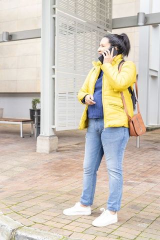 Mature woman talking on smartphone in yellow jacket at urban plaza