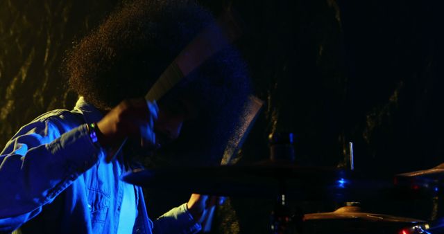 An African American musician is immersed in playing the drums in a dimly lit setting, with copy space. His concentration and the dynamic lighting create an atmosphere of intense musical performance.