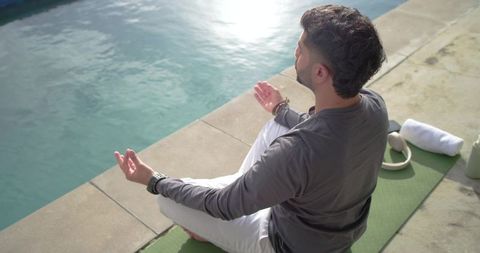 Indian man meditating poolside on yoga mat in sunlight for mindfulness stress relief