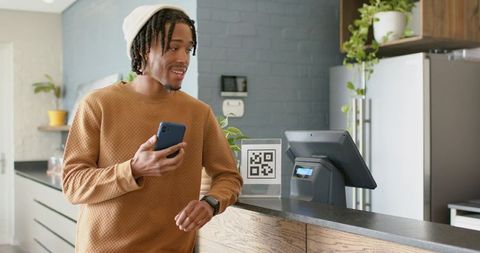 Young african american man scanning qr code at coffeehouse counter with smartphone