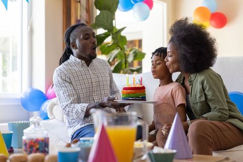 African american family celebrating child birthday blowing out candles on rainbow cake