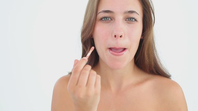 Young woman applying lip gloss while smiling, focusing on beauty and skincare. Ideal for advertising makeup products, beauty tutorials, skincare blogs, or health and wellness visual content.