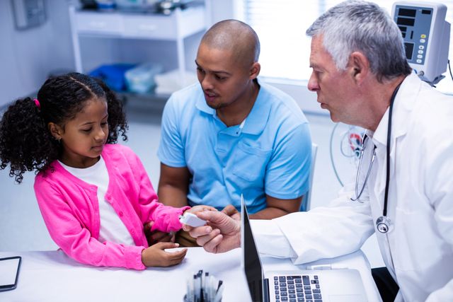 Doctor checking young girl's blood sugar level while father watches. Useful for illustrating healthcare, pediatric care, diabetes management, and family health consultations.