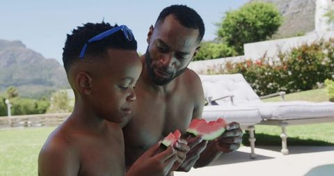African american father and son sharing watermelon poolside summer backyard bonding moment