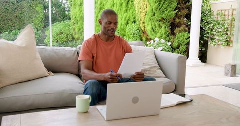 Man Analyzing Documents and Working Remotely on Laptop at Home