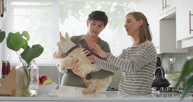 Caucasian lesbian couple holding their dog using smartphone at home. lgbt relationship and lifestyle concept